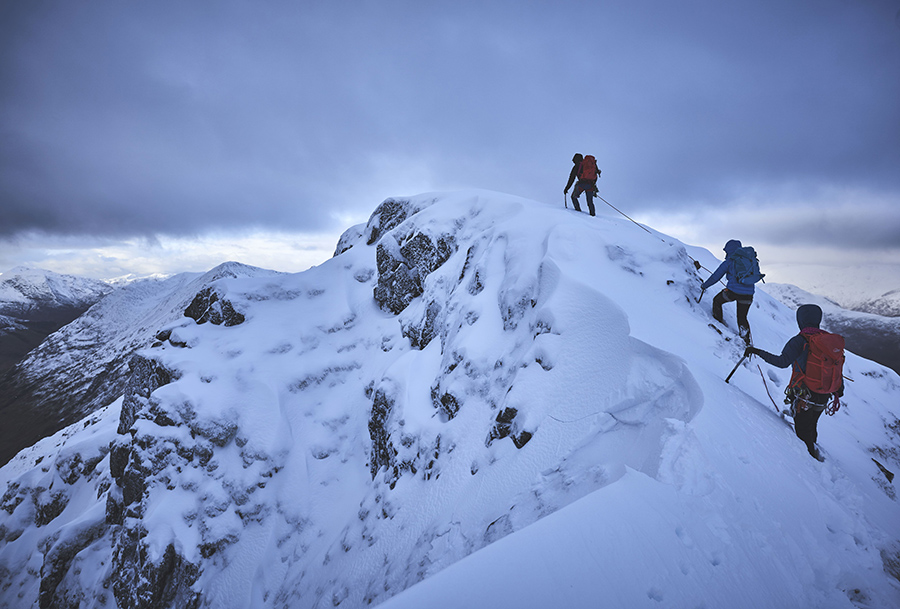 A team of three climbers on a snowy ridge on Aonach Eagach